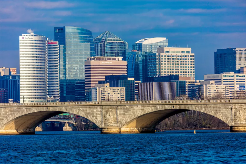Washington D.C. office buildings with river and stone arched bridge in foreground.